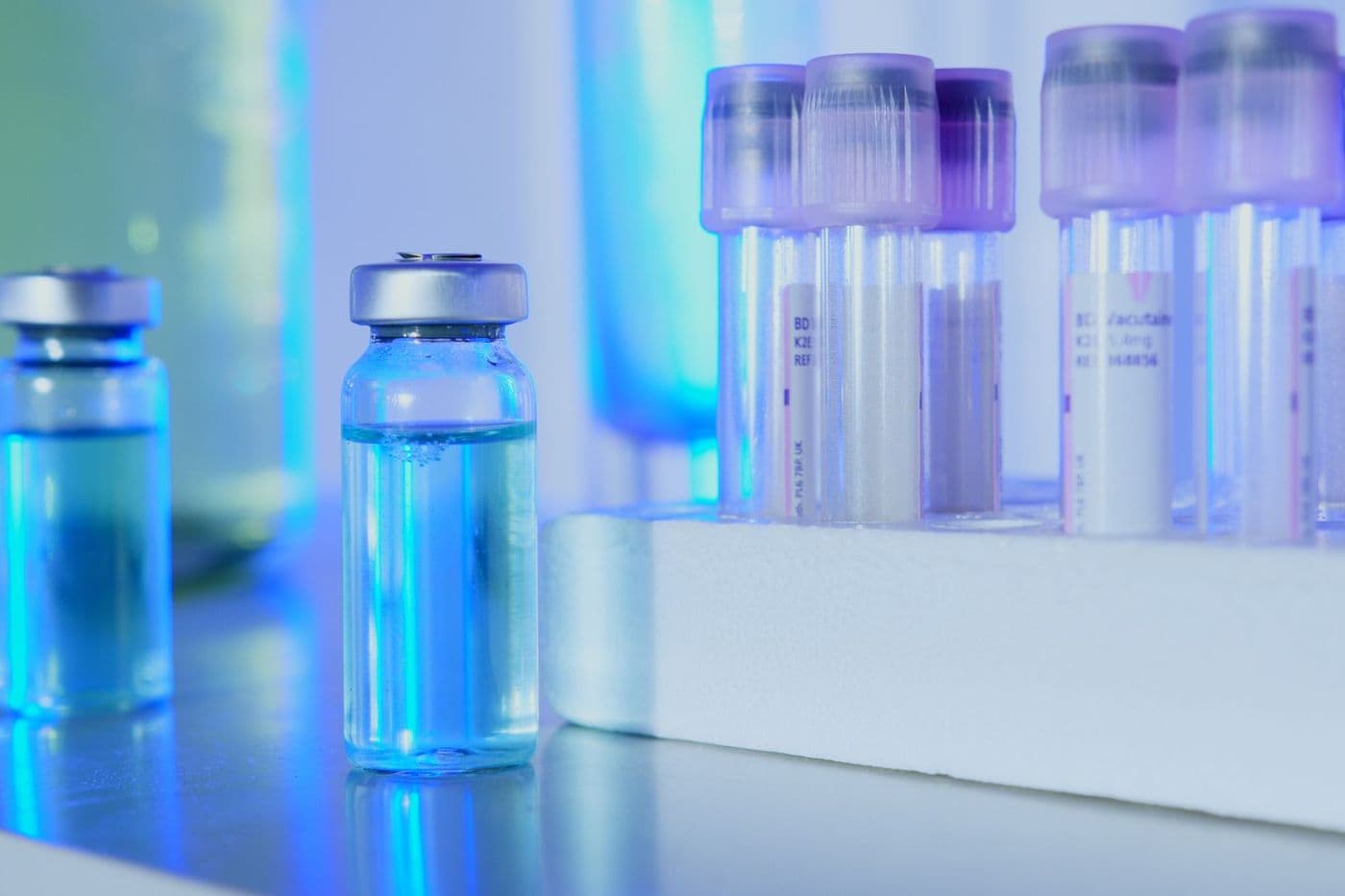 Glass vials and capped tubes under blue laboratory lighting.
